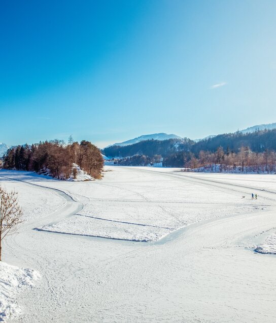 Der Reintalersee in Kramsach, eingebettet in Schnee, auf dem See Spuren für Fußgänger und Eisläufer  | © Alpbachtal Tourismus | Matthias Sedlak 