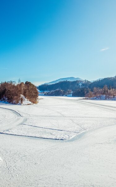 Der Reintalersee in Kramsach, eingebettet in Schnee, auf dem See Spuren für Fußgänger und Eisläufer 
