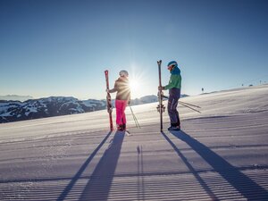 Eine Frau und ein Mann stehen samt Skiausrüstung auf der frisch präparierten Piste, die Sonne scheint und der Schnee glitzert   | © Ski Juwel Alpbachtal Tourismus | shootandstyle 