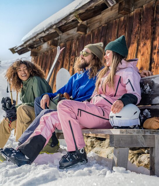 Zwei Frauen und ein Mann sitzen auf einer Bank neben einer Hütte - ihre Ski lehnen an der Hütte. | © Ski Juwel Alpbachtal Wildschönau | Christoph Oberschneider