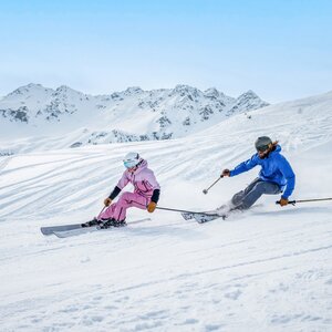 Ein Mann und eine Frau auf der Piste beim Skifahren mit Panorama im Hintergrund. | © Ski Juwel Alpbachtal Wildschönau | Christoph Oberschneider
