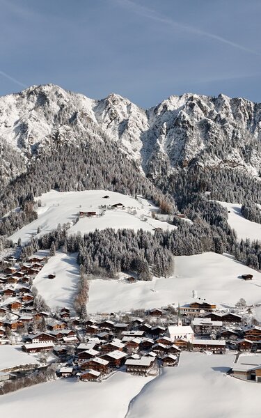 Man sieht das Dorfzentrum Alpbach winterlich verschneit mit den Gipfeln im Hintergrund. | © Alpbachtal Tourismus