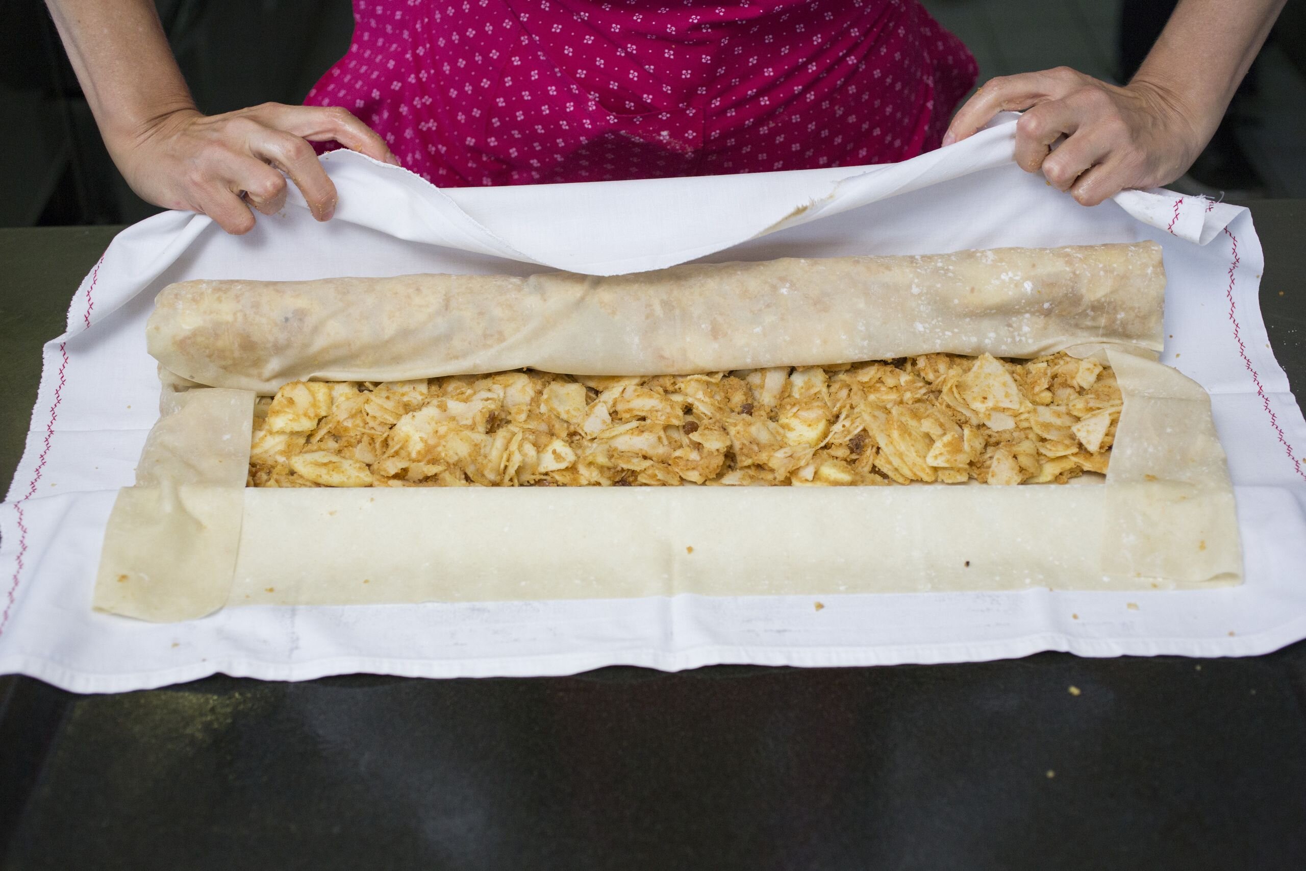 Eine Frau rollt den befüllten Apfelstrudel zu einer Strudelform ein | © Tirol Werbung 