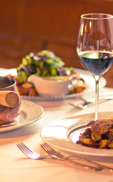 Auf dem Bild sind zwei Weingläser zu sehen, sowie drei Gerichte des Hauses  | © Hotel zur Post Alpbach 