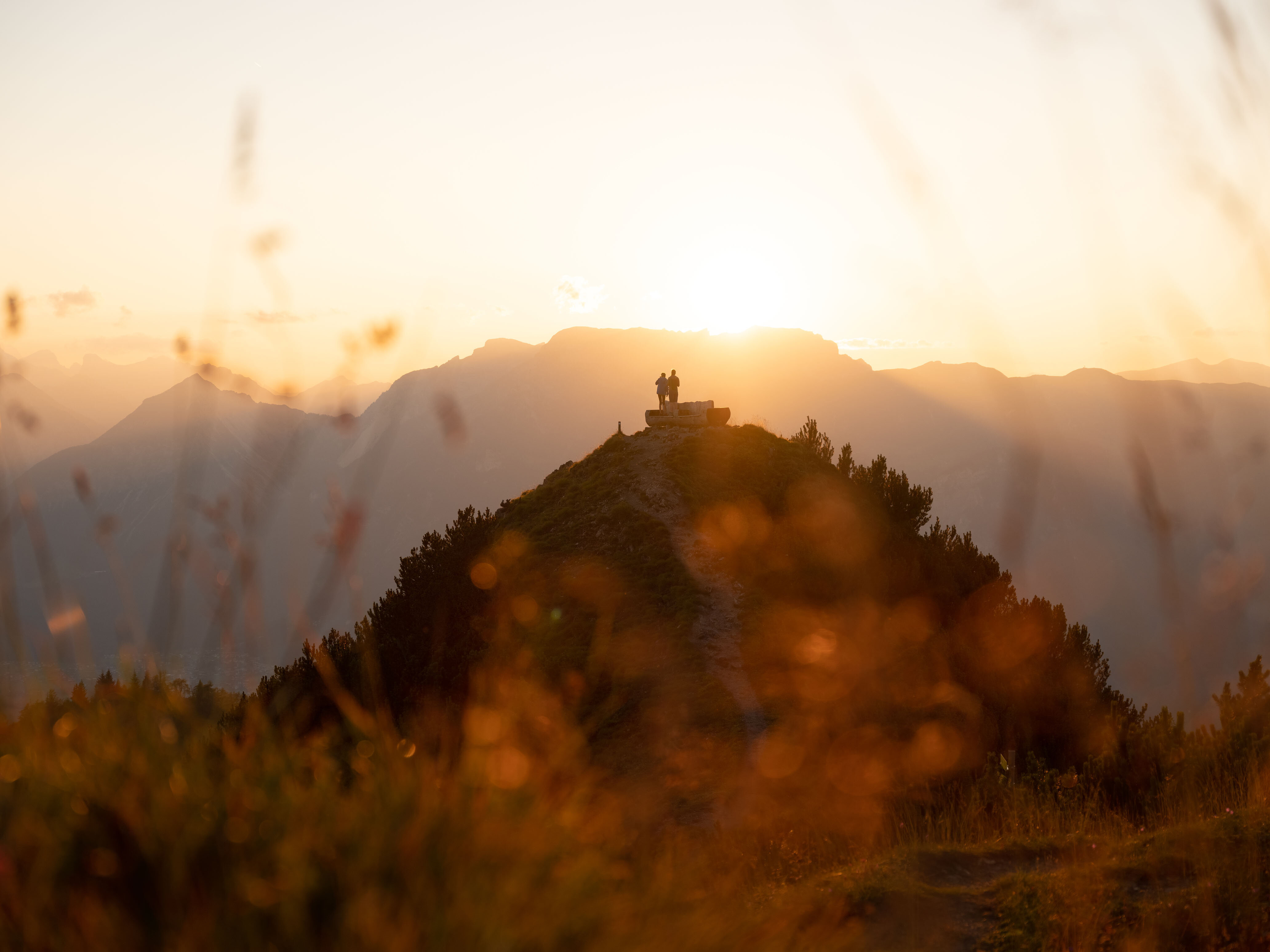 Zwei Personen stehen neben der Rastbank Gratlspitze, sie genießen den wundervollen Sonnenuntergang  | © Alpbachtal Tourismus  | Torsten Mühlbacher 