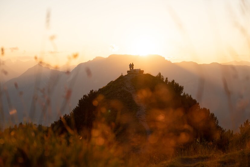 Zwei Personen stehen neben der Rastbank Gratlspitze, sie genießen den wundervollen Sonnenuntergang  | © Alpbachtal Tourismus  | Torsten Mühlbacher 