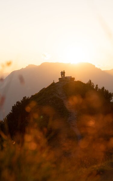 Zwei Personen stehen neben der Rastbank Gratlspitze, sie genießen den wundervollen Sonnenuntergang  | © Alpbachtal Tourismus  | Torsten Mühlbacher 
