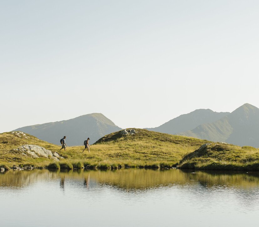 Ein Paar wandert entlang eines Sees, in Richtung des Gipfels Torkopf | © Alpbachtal Tourismus | E. Holzknecht 