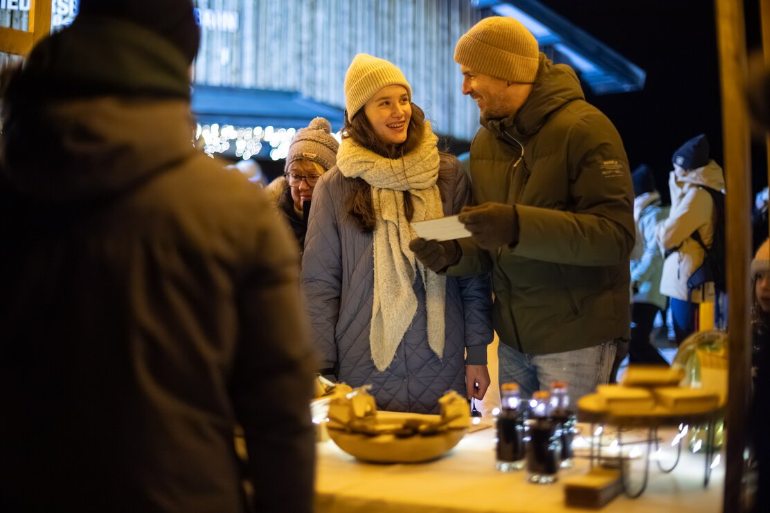 Man sieht ein Pärchen, das gerade freudig etwas bei einem Stand kauft. Es ist gerade Nacht. | © Alpbachtal Tourismus | Maximalgrafik