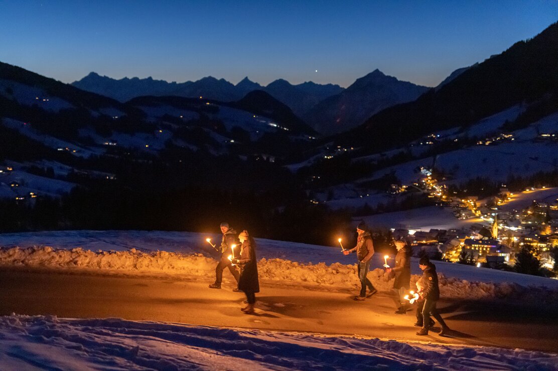 Eine winterliche Fackelwanderung durch Alpbach bei Nacht. Im Hintergrund sieht man das beleuchtete Dorf Alpbach. | © Alpbachtal Tourismus | shootandstyle