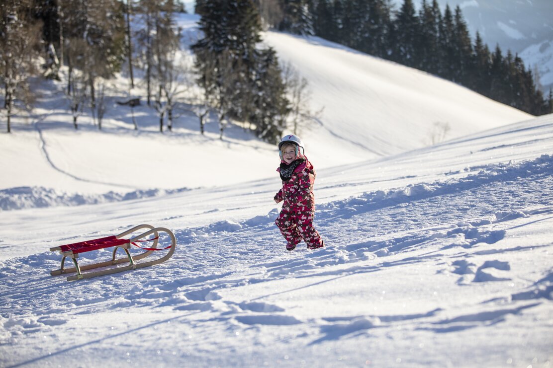 Ein kleines Mädchen im pinken Skianzug läuft gerade zur Rodel, im Hintergrund die weiße Schneelandschaft  | © Alpbachtal Tourismus | shootandstyle
