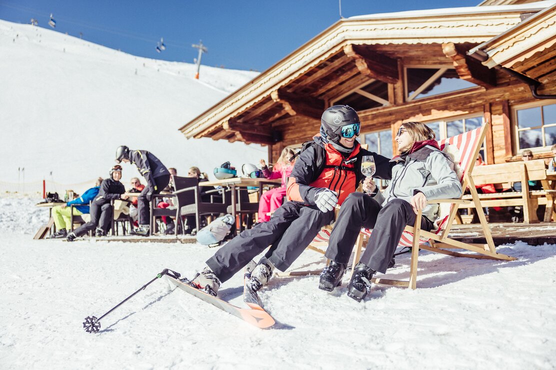 Auf diesem Bild zu sehen ist eine Frau und ein Mann,  sie genießen gerade die Sonne im Liegestuhl, im Hintergrund die Skihütte Kafner Ast in Alpbach | © Alpbachtal Tourismus | shootandstyle 