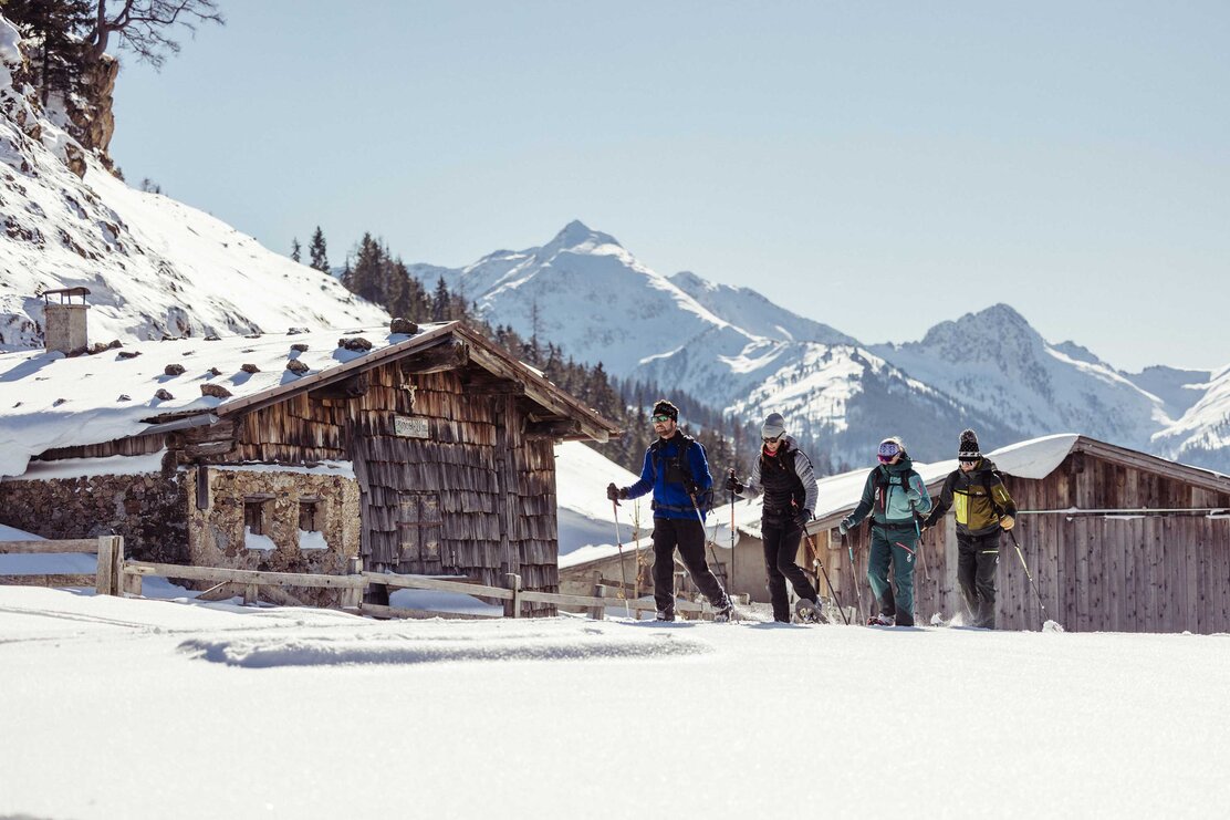 Man sieht eine Gruppe Schneeschuhwanderer in Alpbach, die bei schönem Wetter gerade eine Almhütte passieren. | © Alpbachtal Tourismus | shootandstyle