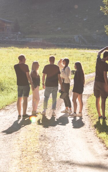 Auf diesem Bild zu sehen sind ein paar Personen, welche auf einer Forststraße stehen und die Sonne genießen, es herrscht eine schöne Lichtstimmung  | © Alpbachtal Tourismus | shootandstyle 